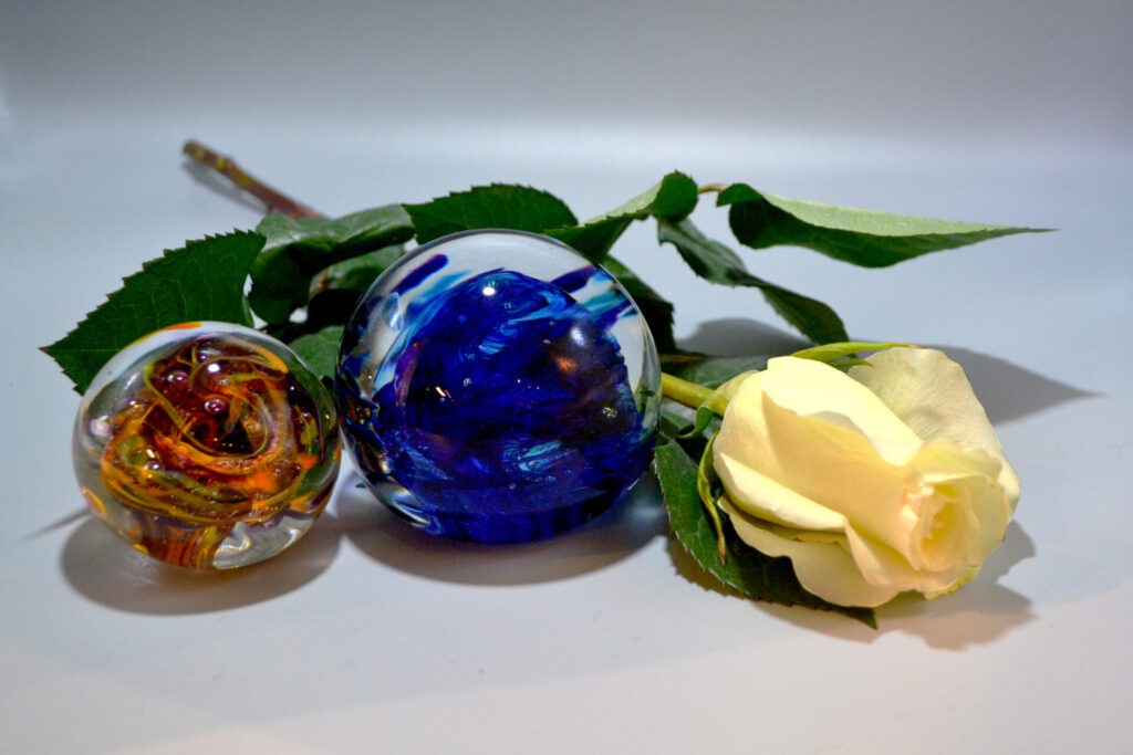 a yellow rose next to two round glass ball paperweights